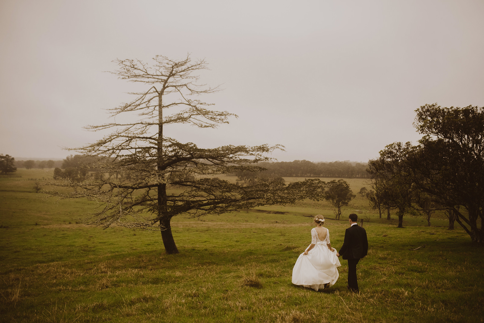 bride and groom on rainy day in field with one tree